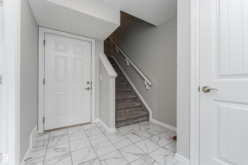 Entryway featuring white panel doors, marble-look floor tiles, carpeted stairs with handrail, and neutral wall paint - #61 215 Saddleback Rd Nw, Edmonton, AB - Indoor Photo Showing Other Room