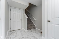 Entryway featuring white panel doors, marble-look floor tiles, carpeted stairs with handrail, and neutral wall paint - 