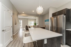 Open-concept kitchen featuring a spacious island with a white countertop, dark wood-finish cabinetry, and recessed lighting - 