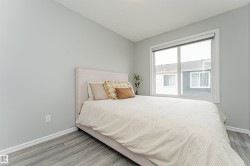 Bright bedroom featuring a large window, neutral gray walls, crisp white trim, and wood-finish flooring - 