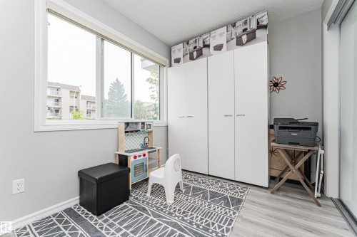 Bright room featuring a large window, light gray walls, wood-finish flooring, and a white built-in wardrobe with multiple panels - #61 215 Saddleback Rd Nw, Edmonton, AB - Indoor Photo Showing Other Room