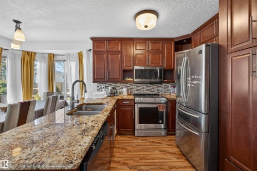 Kitchen featuring wood-finish flooring, rich wood cabinetry, stainless steel appliances, and a mosaic tile backsplash - 9007 169 Avenue Nw, Edmonton, AB - Indoor Photo Showing Kitchen With Double Sink With Upgraded Kitchen