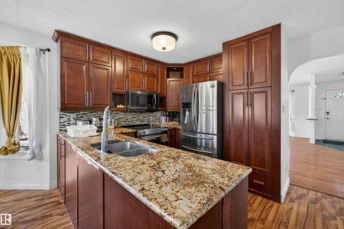 Kitchen featuring wood-finish cabinetry, granite countertops, stainless steel appliances, and a mosaic tile backsplash - 9007 169 Avenue Nw, Edmonton, AB - Indoor Photo Showing Kitchen With Double Sink With Upgraded Kitchen