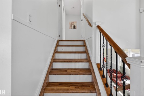 Staircase featuring wood-finish treads, white risers, and a decorative wrought iron baluster railing with a wooden handrail - 9007 169 Avenue Nw, Edmonton, AB - Indoor Photo Showing Other Room