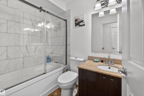 Bathtub with sliding glass enclosure, white subway tile surround, vanity with granite countertop, integrated sink, and modern light fixture - 9007 169 Avenue Nw, Edmonton, AB - Indoor Photo Showing Bathroom