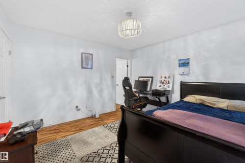 Wood-finish flooring with white walls and a contemporary chandelier - 9007 169 Avenue Nw, Edmonton, AB - Indoor Photo Showing Bedroom