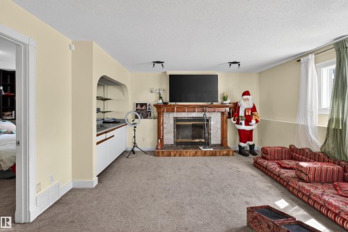 Built-in fireplace with a stone surround and wood mantle, built-in cabinetry with shelving, recessed lighting, and a window with natural light - 9007 169 Avenue Nw, Edmonton, AB - Indoor Photo Showing Living Room With Fireplace