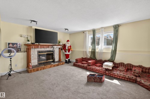 Carpeted room featuring a fireplace with a wood mantel and stone surround, track lighting, and a window with natural light - 9007 169 Avenue Nw, Edmonton, AB - Indoor Photo Showing Living Room With Fireplace