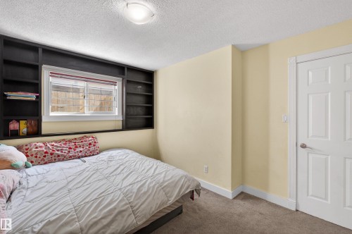 Built-in shelving surrounding a window, paneled interior door, ceiling-mounted light fixture, and textured ceiling - 9007 169 Avenue Nw, Edmonton, AB - Indoor Photo Showing Bedroom
