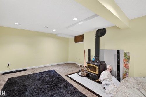 Carpeted room featuring a wood-burning stove with a tiled hearth and a black flue - 9007 169 Avenue Nw, Edmonton, AB - Indoor