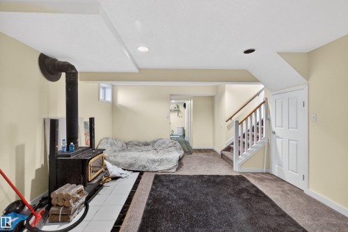 Carpeted flooring, recessed lighting, white trim, wood-burning stove with a tiled base, and a white paneled door - 9007 169 Avenue Nw, Edmonton, AB - Indoor Photo Showing Other Room