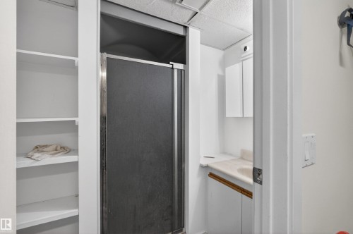 Built-in shelving, shower enclosure with chrome trim, vanity with integrated sink, white cabinetry, and wall-mounted storage cabinet - 9007 169 Avenue Nw, Edmonton, AB - Indoor