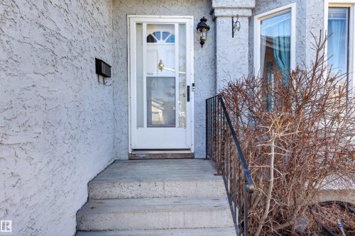 Stucco exterior with a storm door, concrete entry stairs, and a black wrought iron handrail - 9007 169 Avenue Nw, Edmonton, AB - Outdoor