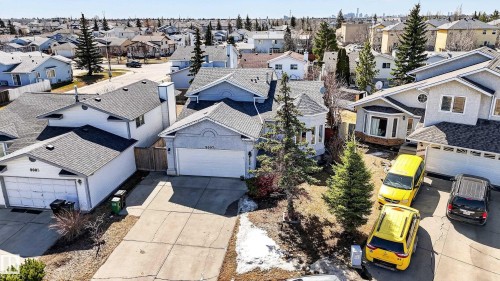 Exterior featuring a light grey stucco finish, a two-car garage, an asphalt shingle roof, mature evergreen trees, and a concrete driveway - 9007 169 Avenue Nw, Edmonton, AB - Outdoor