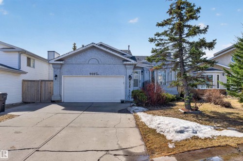 Stucco exterior with an attached garage, paved driveway, and mature landscaping - 9007 169 Avenue Nw, Edmonton, AB - Outdoor