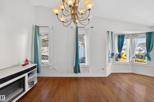 Vaulted ceiling with an ornate chandelier, wood-finish flooring, built-in media console with an electric fireplace, and a bay window - 9007 169 Avenue Nw, Edmonton, AB - Indoor Photo Showing Other Room
