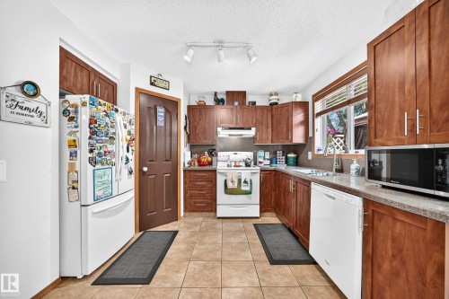 Kitchen featuring wood-finish cabinetry, tile flooring, track lighting, and a double-basin sink - 13069 37 Street Nw, Edmonton, AB - Indoor Photo Showing Kitchen