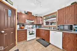 Kitchen featuring wood-finish cabinetry, tile flooring, solid surface countertops, and an integrated white dishwasher - 