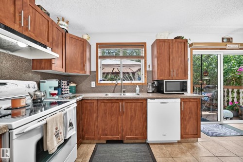 Kitchen featuring wood cabinetry, stone-finish countertops, tile flooring, and a sliding glass door - 13069 37 Street Nw, Edmonton, AB - Indoor Photo Showing Kitchen With Double Sink