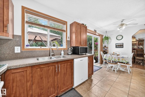 Kitchen featuring wood cabinetry, a stainless steel double basin sink, a large window, a sliding glass door, and tile flooring - 13069 37 Street Nw, Edmonton, AB - Indoor Photo Showing Kitchen With Double Sink