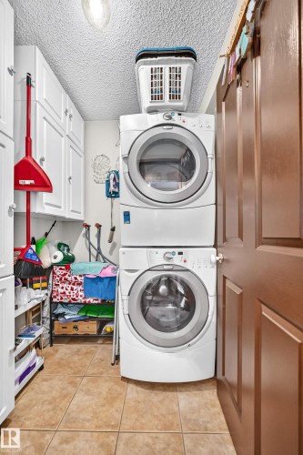 Compact laundry area featuring a stacked washer and dryer, white shaker-style cabinetry, and tile flooring - 13069 37 Street Nw, Edmonton, AB - Indoor Photo Showing Laundry Room