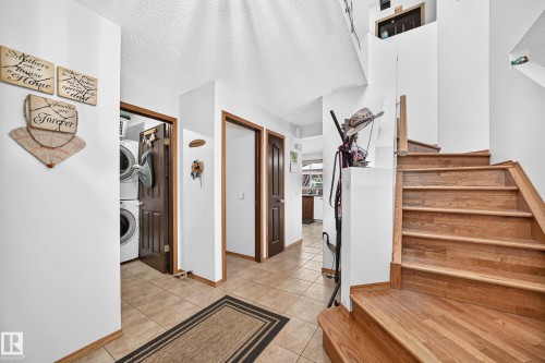 Wood-finish staircase, tile flooring, white walls, dark wood-finish doors, and a laundry closet with stacked appliances - 13069 37 Street Nw, Edmonton, AB - Indoor Photo Showing Other Room