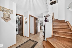 Wood-finish staircase, tile flooring, white walls, dark wood-finish doors, and a laundry closet with stacked appliances - 
