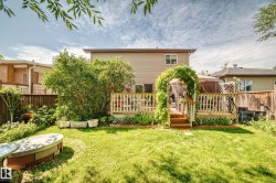 Expansive backyard featuring a manicured lawn, a multi-level wood deck, a vine-covered archway, mature landscaping, and a built-in fire pit - 