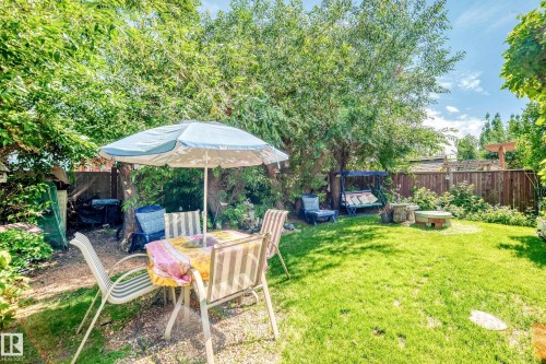 Manicured lawn with mature trees, wood fencing, and a built-in stone fire pit area - 13069 37 Street Nw, Edmonton, AB - Outdoor With Deck Patio Veranda With Backyard