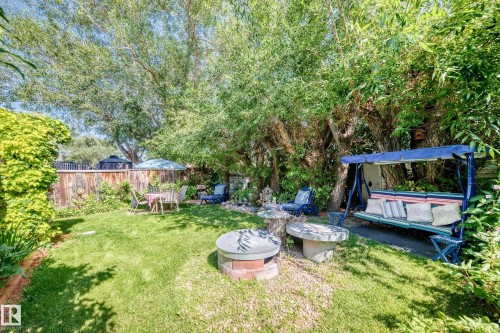 Expansive yard featuring a manicured lawn, mature trees, a wood privacy fence, and a stone-clad fire pit with a concrete cap - 13069 37 Street Nw, Edmonton, AB - Outdoor