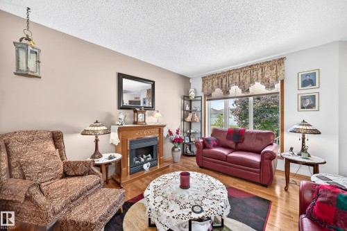 Recessed fireplace with a wood mantel, hardwood flooring, and large picture windows - 13069 37 Street Nw, Edmonton, AB - Indoor Photo Showing Living Room With Fireplace