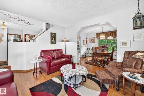Hardwood flooring extends throughout the living area, featuring a half-wall partition and an arched entryway to the dining space - 13069 37 Street Nw, Edmonton, AB - Indoor Photo Showing Living Room