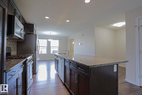 Kitchen featuring dark wood-finish cabinetry, stainless steel appliances, granite countertops, and a tile backsplash - 308 Watt Boulevard Sw, Edmonton, AB - Indoor Photo Showing Kitchen With Upgraded Kitchen