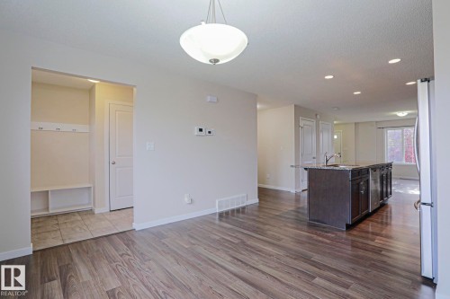 Open-concept living area featuring wood-finish flooring, recessed lighting, a modern pendant light, and a kitchen island with built-in cabinetry and an integrated sink - 308 Watt Boulevard Sw, Edmonton, AB - Indoor