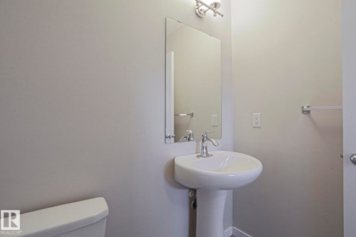 Pedestal sink with chrome faucet, rectangular mirror, and wall-mounted light fixture - 308 Watt Boulevard Sw, Edmonton, AB - Indoor Photo Showing Bathroom