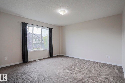 Neutral wall paint, textured carpeting, large window with white trim, and a ceiling-mounted light fixture - 308 Watt Boulevard Sw, Edmonton, AB - Indoor Photo Showing Other Room