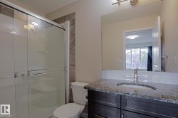 Shower with glass enclosure, single vanity with granite countertop, white subway tile backsplash, and a wall-mounted mirror - 