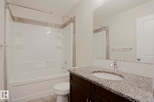 Bathroom featuring a shower-tub combination, vanity with a granite-style countertop, integrated sink, and large wall-mounted mirror - 308 Watt Boulevard Sw, Edmonton, AB - Indoor Photo Showing Bathroom