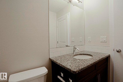 Vanity with a polished chrome faucet, under-mount sink, and speckled countertop, white subway tile backsplash, and a wall-mounted mirror - 308 Watt Boulevard Sw, Edmonton, AB - Indoor Photo Showing Bathroom