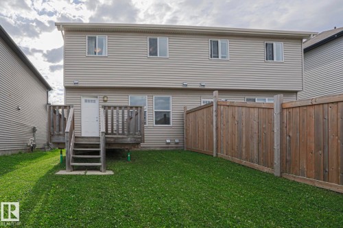 Rear exterior with light-colored siding, multiple windows, a wooden deck with stairs, a white exterior door, and a wooden privacy fence - 308 Watt Boulevard Sw, Edmonton, AB - Outdoor With Exterior