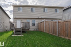 Rear exterior with light-colored siding, multiple windows, a wooden deck with stairs, a white exterior door, and a wooden privacy fence - 