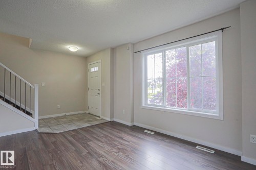 Wood-finish flooring, tiled entry, white interior door with lites, staircase with white newel post and dark balusters, and a large window with white framing - 308 Watt Boulevard Sw, Edmonton, AB - Indoor Photo Showing Other Room