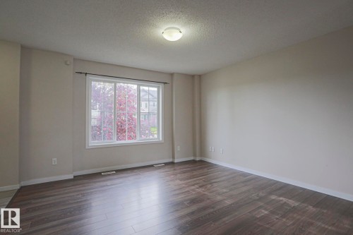 Spacious room featuring wood-finish flooring, a large multi-pane window, and neutral wall tones - 308 Watt Boulevard Sw, Edmonton, AB - Indoor Photo Showing Other Room