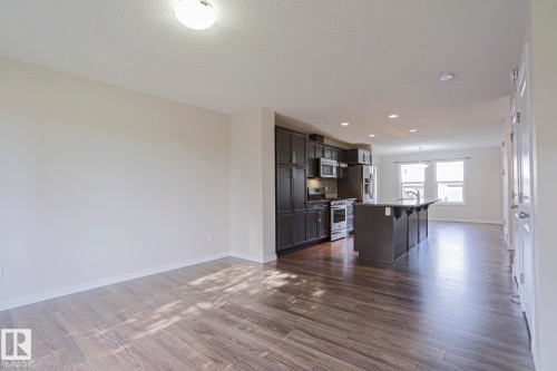 Wood-finish flooring throughout, kitchen featuring dark wood cabinetry, stainless steel appliances, and an island with bar seating - 308 Watt Boulevard Sw, Edmonton, AB - Indoor
