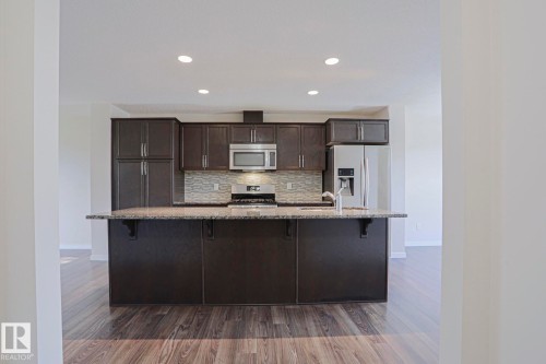 Kitchen featuring dark wood cabinetry, stainless steel appliances, a mosaic tile backsplash, and wood-finish flooring - 308 Watt Boulevard Sw, Edmonton, AB - Indoor Photo Showing Kitchen With Upgraded Kitchen