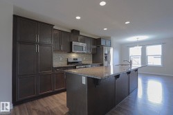 Kitchen featuring dark wood-finish cabinetry, stainless steel appliances, a tiled backsplash, a kitchen island with stone countertops, and wood-finish flooring - 