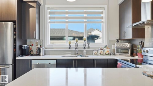 Contemporary kitchen featuring dark wood-finish cabinetry, stainless steel appliances, white countertops, and a light gray subway tile backsplash - 731 36 Street Sw, Edmonton, AB - Indoor Photo Showing Kitchen With Double Sink With Upgraded Kitchen