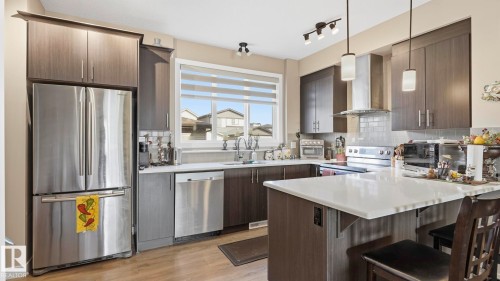 Modern kitchen featuring stainless steel appliances, dark wood-finish cabinetry, a subway tile backsplash, a bright window, and a central island with a light-toned countertop - 731 36 Street Sw, Edmonton, AB - Indoor Photo Showing Kitchen With Upgraded Kitchen