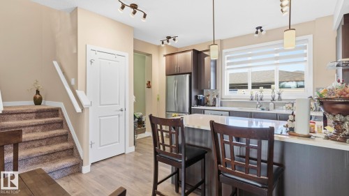 Modern kitchen with stainless steel appliances, dark wood-finish cabinetry, and a light-toned countertop island with seating - 731 36 Street Sw, Edmonton, AB - Indoor