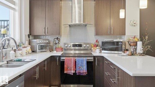 U-shaped kitchen featuring wood-grain cabinetry, white countertops, stainless steel appliances, and a tiled backsplash - 731 36 Street Sw, Edmonton, AB - Indoor Photo Showing Kitchen With Double Sink With Upgraded Kitchen